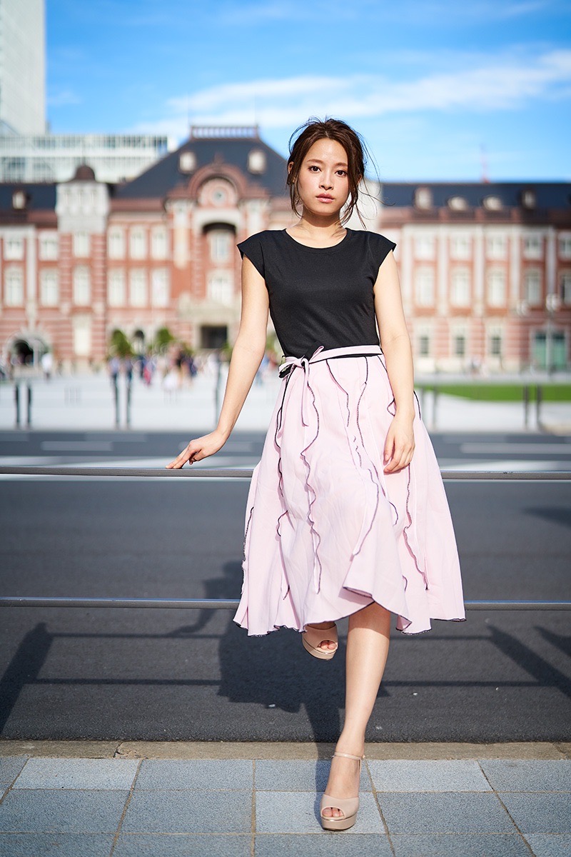 駅舎を背景に立つ女性の全身ポートレート